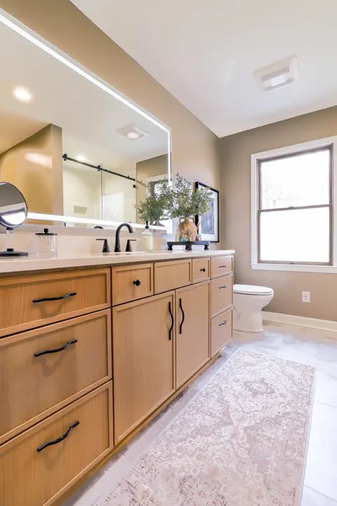 Bathroom with a long blonde wood vanity and a large lit mirror