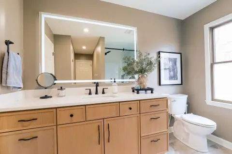 Bathroom with a light blonde wood vanity, white top and lit mirror
