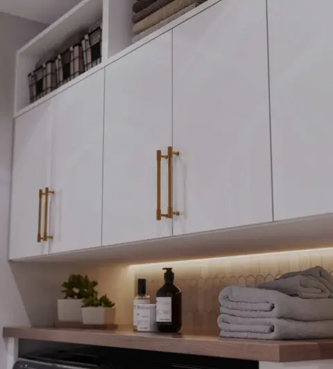 Close-up of white cabinet doors with long brass bar pulls over a lit shelf