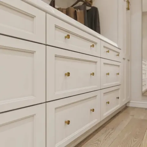 Close-up of white paneled drawer fronts with round brass knobs