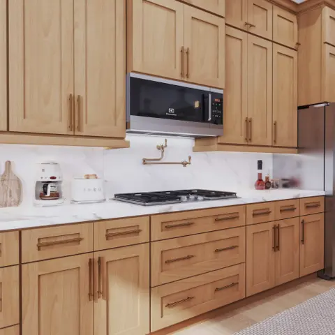 Kitchen with honey-toned wood shaker cabinets, brass pulls and a white stone backsplash
