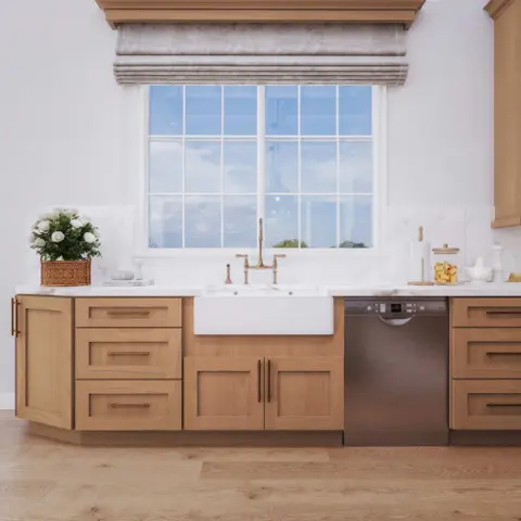Sink wall of natural wood base cabinets with a farmhouse sink under a window